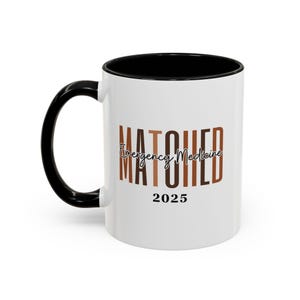 May include: White ceramic coffee mug with a black rim and handle. The mug has the text "MATCHED" in brown and black letters with the words "Emergency Medicine" in cursive script below. The year "2025" is printed in black below the text.