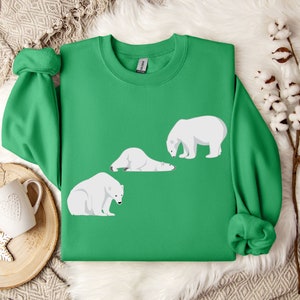 Peut inclure: Un sweat-shirt vert avec un motif de trois ours polaires blancs dans diff&eacute;rentes poses. Les ours sont tous tourn&eacute;s dans la m&ecirc;me direction, et le sweat-shirt a un col rond.