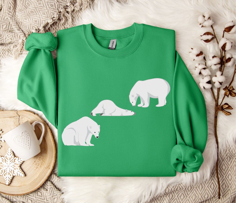 Peut inclure: Un sweat-shirt vert avec un motif de trois ours polaires blancs dans diff&eacute;rentes poses. Les ours sont tous tourn&eacute;s dans la m&ecirc;me direction, et le sweat-shirt a un col rond.