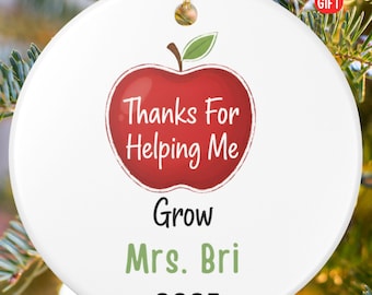 May include: White ceramic ornament with a red apple design and the text "Thanks For Helping Me Grow Mrs. Bri 2025". The ornament has a gold string for hanging and is a personalized gift.