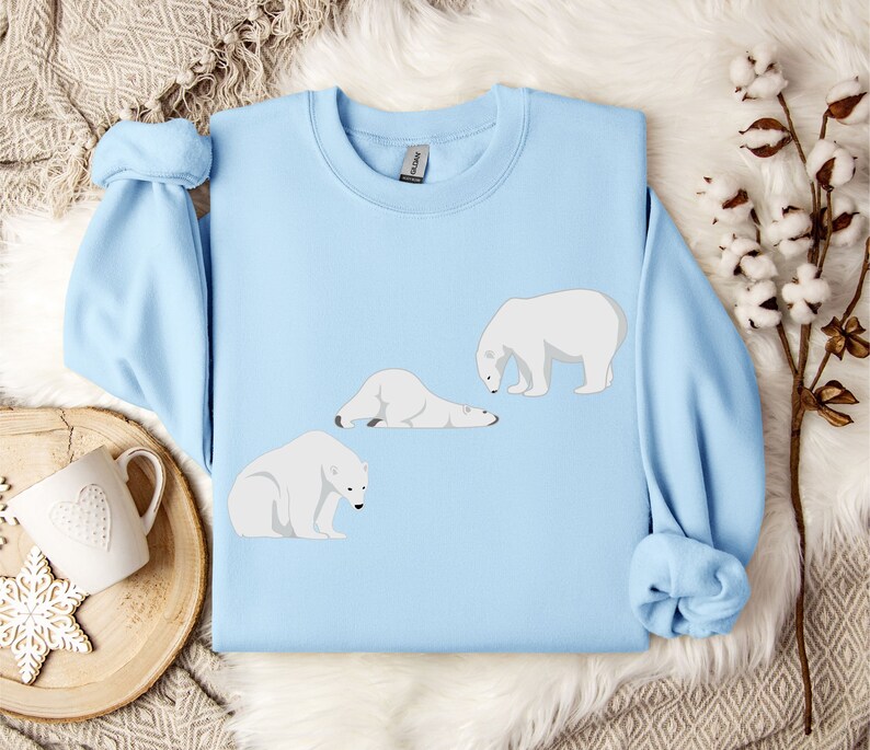 Peut inclure: Un sweat-shirt bleu clair avec un motif de trois ours polaires. Un ours est debout, un autre est couch&eacute; et le dernier est assis. Les ours sont tous blancs.