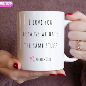 May include: White ceramic mug with black text that reads "I love you because we hate the same stuff". Below the text are two pink hearts and the text "Rachel + Grey".