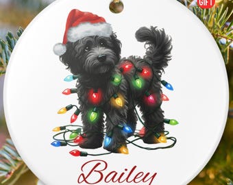 May include: A round, white Christmas ornament featuring a black dog wearing a Santa hat and wrapped in colorful Christmas lights. The name "Bailey" and the year "2025" are written in red script. The words "PERSONALIZED GIFT" are in the upper right corner.