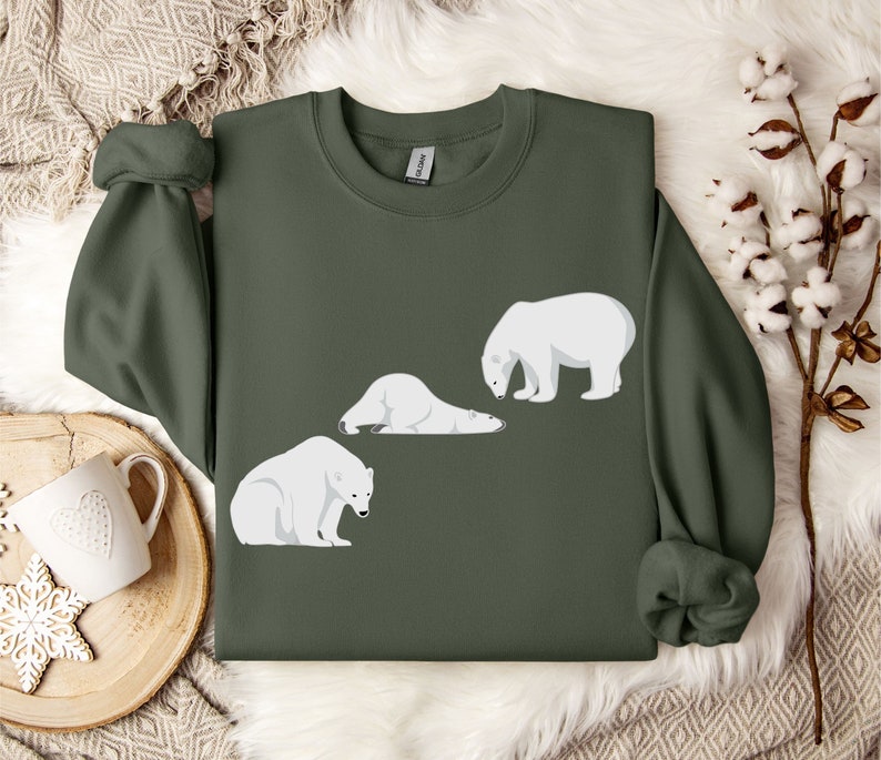 Peut inclure: Un sweat-shirt vert fonc&eacute; avec un motif blanc de trois ours polaires. Les ours sont dans des poses diff&eacute;rentes, l'un est couch&eacute;, l'autre est debout et regarde vers le bas, et le dernier est debout et regarde sur le c&ocirc;t&eacute;.