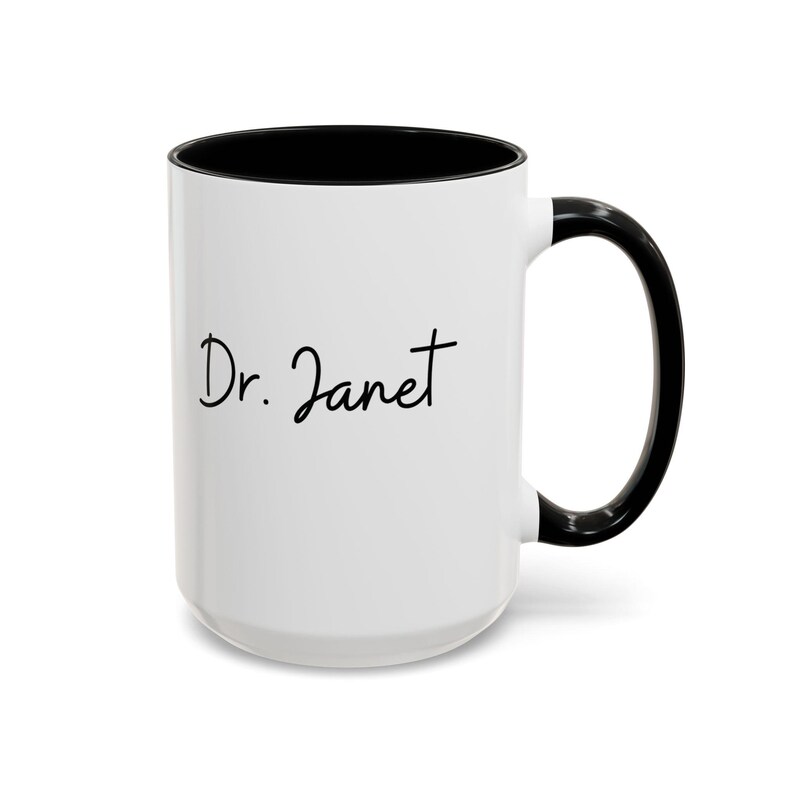May include: White ceramic coffee mug with a black rim and handle. The mug has the text "Dr. Janet" written in black cursive.
