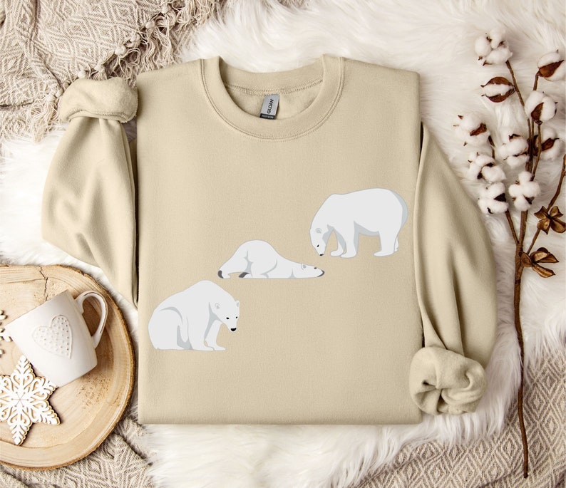 Peut inclure: Un sweat-shirt beige avec un motif de trois ours polaires blancs dans diff&eacute;rentes poses. Les ours sont tous tourn&eacute;s dans la m&ecirc;me direction, et le sweat-shirt a un col rond.