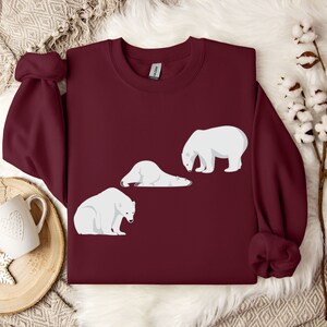 Peut inclure: Un sweat-shirt bordeaux avec un motif de trois ours polaires blancs. Deux des ours sont couch&eacute;s et un est debout.