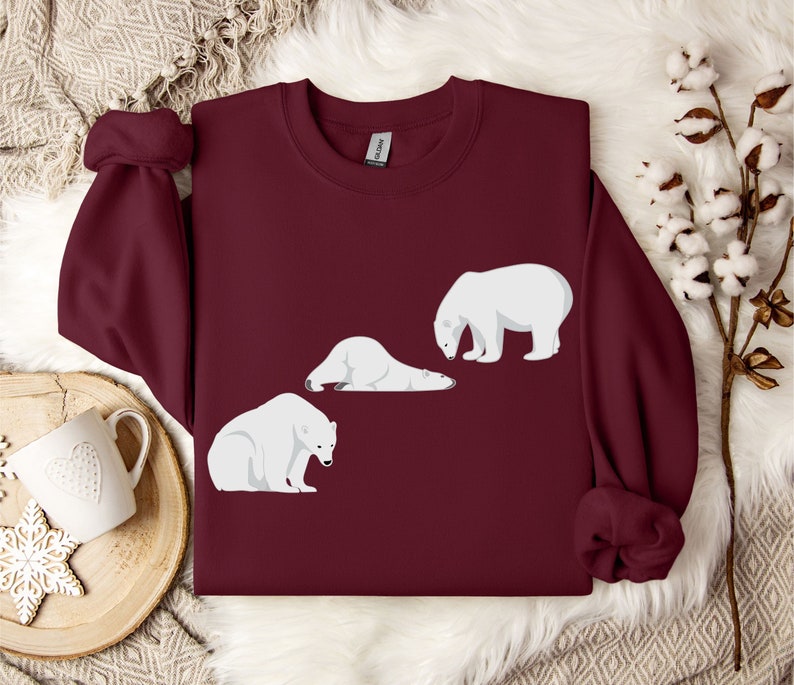Peut inclure: Un sweat-shirt bordeaux avec un motif de trois ours polaires blancs. Deux des ours sont couch&eacute;s et un est debout.