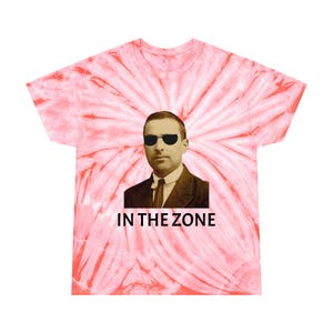 May include: A pink tie-dye t-shirt with a black and white image of a man wearing sunglasses and a suit. The text "IN THE ZONE" is printed below the image.