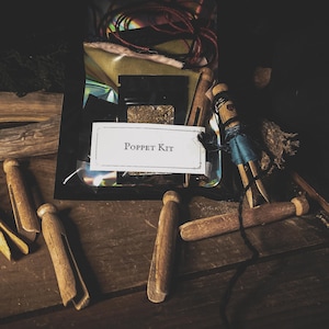 May include: A Poppet Kit with wooden clothespins, a small doll, and various craft supplies. The kit includes a label that reads "Poppet Kit". The items are arranged on a dark wooden surface.