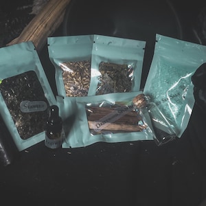 May include: An assortment of natural products, including seaweed, herbs, and sea salt, packaged in light blue pouches. A small glass bottle with a dropper and a cork-topped vial of driftwood are also present. The word "Seaweed" is visible on one pouch.