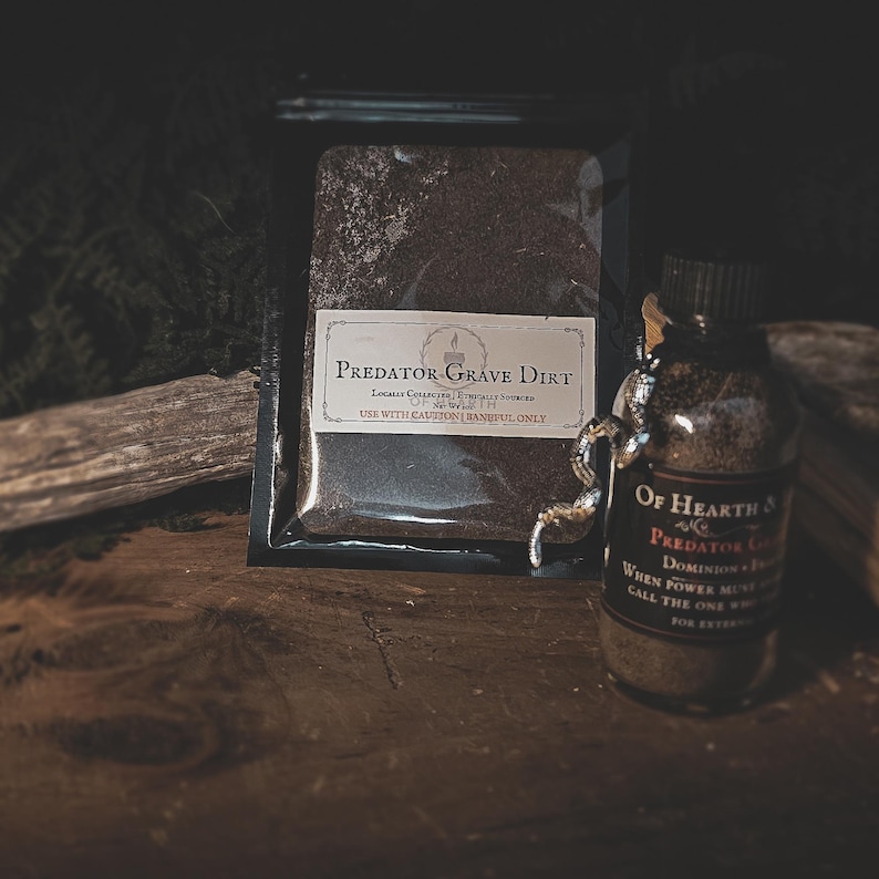 May include: A dark, moody image featuring a small glass bottle and a sealed bag, both filled with dark brown material labeled "Predator Grave Dirt." The bottle has a decorative silver snake. The bag has a white label with text.