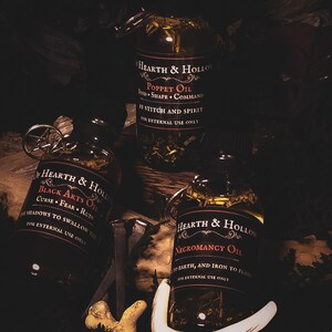Peut inclure: Trois flacons en verre d'huiles Hearth & Hollow avec des &eacute;tiquettes sombres et des accents argent&eacute;s. Les &eacute;tiquettes indiquent "Poppet Oil", "Black Arts Oil" et "Necromancy Oil". Chaque bouteille contient des herbes et des huiles.