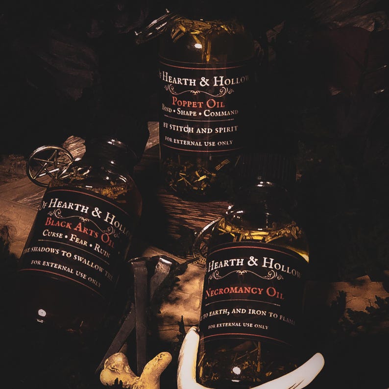 Peut inclure: Trois flacons en verre d'huiles Hearth & Hollow avec des &eacute;tiquettes sombres et des accents argent&eacute;s. Les &eacute;tiquettes indiquent "Poppet Oil", "Black Arts Oil" et "Necromancy Oil". Chaque bouteille contient des herbes et des huiles.