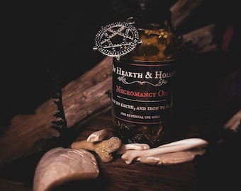 Peut inclure: Image sombre d'une bouteille d'"Huile de nécromancie" avec un charme pentagramme. La bouteille, étiquetée "Hearth & Hollow", contient des herbes. Des fragments d'os et une grosse pierre sont disposés sur une surface en bois.
