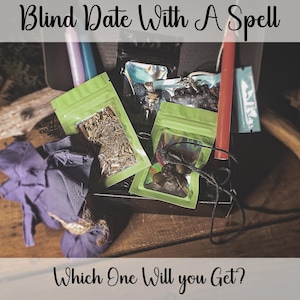 May include: A wooden box with the text "Blind Date With A Spell" and "Which One Will you Get?" contains various items. These include green pouches, a red candle, a purple cloth, and small glass bottles. The contents of the pouches are not visible.