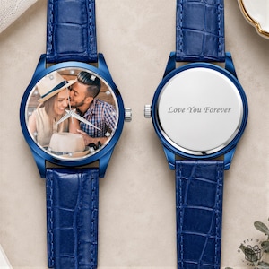 May include: A blue wristwatch with a textured leather strap and a round face featuring a photograph of a couple. The watch face has small crystal markers. A second watch case is shown with a silver back engraved with the text Love You Forever.