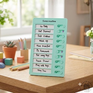 Op de afbeelding: Een mintgroene Luna-routinechecklist met een lijst met taken, waaronder "Go Potty", "Get Dressed" en "Story Time". De checklist heeft tuimelschakelaars om taken als voltooid te markeren. De checklist staat op een houten tafel.