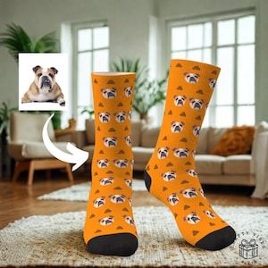 Peut inclure: Une paire de chaussettes orange avec un motif répété de visages de bouledogues et de formes triangulaires marron. Les chaussettes ont des orteils et des talons noirs. L'image comprend également une photo d'un bouledogue.