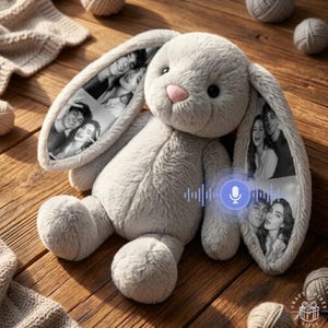 May include: A plush gray rabbit stuffed animal with long ears featuring printed black and white photographic collages of people. The rabbit has a soft, fuzzy texture, dark eyes, and a small pink nose. A blue circular microphone icon is visible.