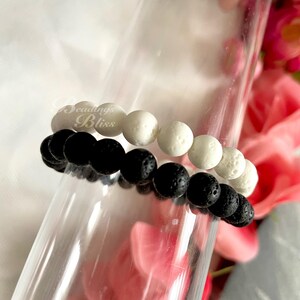 May include: Two beaded bracelets, one black and one white. The black bracelet is made of lava rock beads and the white bracelet is made of white stone beads.