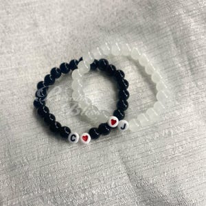 May include: Two beaded bracelets, one black and one white, with red heart charms and the letters "C" and "J" on them.