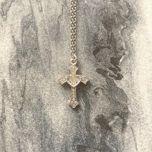 May include: A silver cross necklace with clear rhinestones. The cross is detailed with a heart in the center.