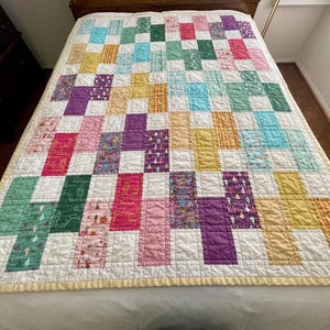 May include: A patchwork quilt with a white background and squares of various colors, including pink, purple, green, yellow, and blue. The quilt is made of different fabrics with various patterns.