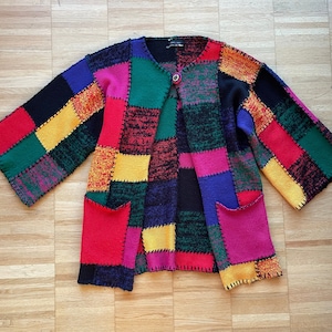 Può includere: Un cardigan colorato a patchwork con chiusura a bottone. Il cardigan è realizzato in un tessuto morbido e lavorato a maglia e presenta una varietà di colori, tra cui rosso, giallo, blu, verde e nero.