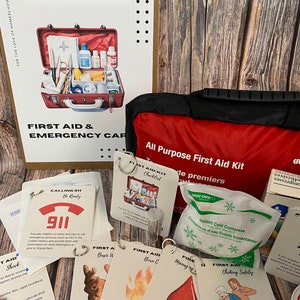 Puede incluir: Una bolsa roja de primeros auxilios con asa y cremallera negras. La bolsa está etiquetada como "Botiquín de primeros auxilios para todo uso". Hay varias tarjetas con instrucciones de primeros auxilios, que incluyen "Lista de verificación del botiquín de primeros auxilios", "Llamar al 911", "Primeros auxilios para heridas básicas", "Primeros auxilios para quemaduras C", "Manejo de hemorragias severas", "Seguridad de primeros auxilios para la asfixia", y "Compresa fría instantánea".