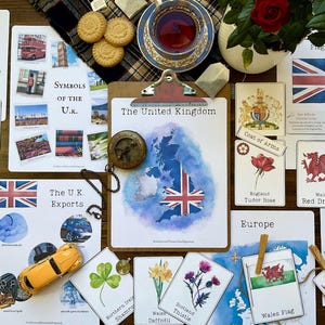 May include: A collection of educational flashcards about the United Kingdom. The cards feature symbols, flags, and other information about England, Scotland, Wales, and Northern Ireland. The cards are laid out on a wooden table with a cup of tea and other items.