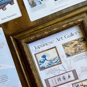 May include: A framed print of a Japanese woodblock print titled 'The Great Wave of Kanagawa' by Katsushika Hokusai. The print is surrounded by other Japanese art prints and a small piece of paper with Japanese text that reads '館命立'. The frame is gold and has a decorative design. The background is a light pink with a floral pattern.