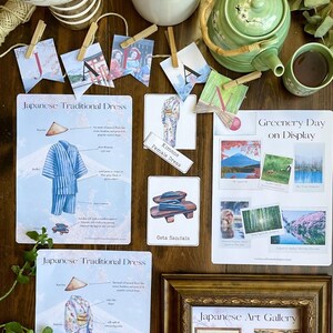 May include: A collection of Japanese themed educational posters. The posters are printed on white paper with colorful illustrations and text. The posters include information about traditional Japanese dress, geta sandals, and greenery day. The posters are displayed on a wooden surface with a globe, a teapot, and a cup of tea.