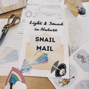 May include: An assortment of educational materials with the theme "Light & Sound in Nature." Includes a "SNAIL MAIL" envelope, stickers, a lightbulb illustration, and a pair of gold scissors. The materials are arranged on a wooden surface.