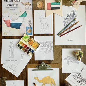 May include: A collection of coloring sheets and art supplies on a wooden surface. The sheets feature illustrations of Arabian animals, traditional clothing, and the United Arab Emirates. A watercolor palette and colored pencils are also present.