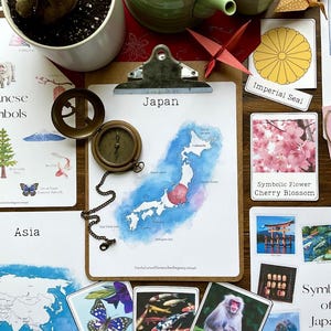 May include: A watercolor illustration of Japan with a blue and white color scheme. The illustration is surrounded by flashcards with images and text about Japan. The flashcards include images of a cherry blossom, a koi fish, a Japanese macaque, a torii gate, and a Japanese imperial seal. The text on the flashcards reads: 'Symbolic Flower Cherry Blossom', 'Symbolic Fish Koi Fish', 'Symbolic Animal Japanese Macaque', 'Imperial Seal', and 'Symbolic Flower Cherry Blossom'. The text on the map reads: 'Japan'.