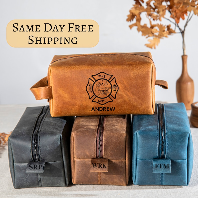 May include: Four leather toiletry bags, one brown with a firefighter emblem and the name "Andrew" engraved, one brown with "WRK" engraved, one blue with "FTM" engraved, and one dark blue with "SRP" engraved.