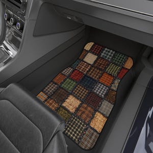 Può includere: Un tappetino per auto con un design patchwork. Il tappetino presenta una varietà di quadrati di tessuto in tonalità di marrone, rosso, verde e blu, creando un aspetto rustico e trapuntato. Il tappetino è posto all'interno di un'auto.
