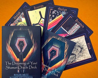 May include: The Dreaming of You! Shaman Oracle Deck by Roger Metz, featuring a box and guidebook with a dark, illustrated cover showing a figure and geometric shapes, surrounded by several individual oracle cards labeled Shalak, Buenga, Azelyn, Bongala, and Kinja.