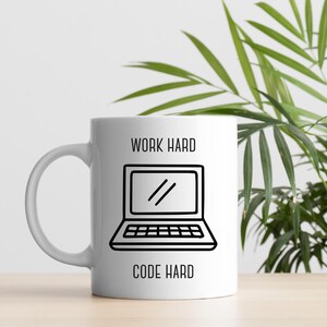 May include: White ceramic mug with a black line drawing of a laptop. The words "WORK HARD" and "CODE HARD" are printed in black, stacked above and below the laptop graphic. The mug has a curved handle.