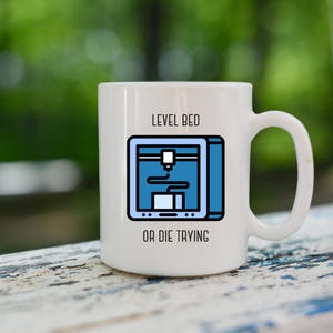 May include: White ceramic mug featuring a blue and black illustration of a 3D printer with the text "LEVEL BED OR DIE TRYING". The mug has a curved handle and is suitable for hot or cold beverages.