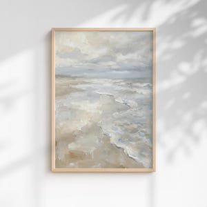 Pode incluir: Pintura emoldurada de uma cena de praia. A obra retrata um céu nublado sobre o oceano, com ondas quebrando na costa. A paleta de cores é suave, com tons de bege, cinza e azul. A pintura está em uma moldura de madeira clara.