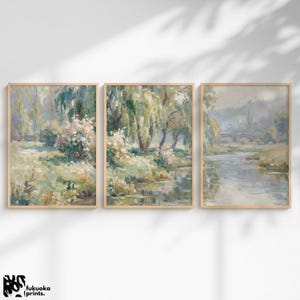 May include: A triptych of framed landscape paintings. Each artwork depicts a tranquil, impressionistic scene with trees, water, and a soft palette of greens, blues, and creams. The art is presented in light-coloured wooden frames, creating a harmonious look.