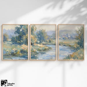 Pode incluir: Conjunto de três pinturas de paisagens emolduradas. Cada uma apresenta uma cena de rio com árvores e folhagens em tons de azul, verde e bege. A obra de arte tem um estilo suave e impressionista, com pinceladas visíveis. As molduras são de madeira clara.