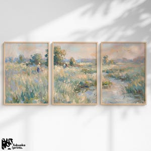 Könnte beinhalten: Set aus drei gerahmten Landschaftskunst-Drucken. Jeder Druck zeigt ein pastellfarbenes impressionistisches Gemälde eines Feldes mit hohem Gras, Bäumen und Figuren. Das Kunstwerk befindet sich in einem hellen Holzrahmen.