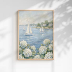 Pode incluir: Uma pintura emoldurada retrata veleiros num mar azul, com flores brancas em primeiro plano. A obra de arte tem uma moldura de madeira clara e um tema costeiro sereno. O céu é azul claro com nuvens.