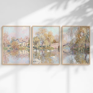May include: Set of three framed landscape art prints. The artwork features a serene river scene with a house, bridge, and swans. The color palette includes soft pinks, blues, and greens, creating a calming and picturesque aesthetic.