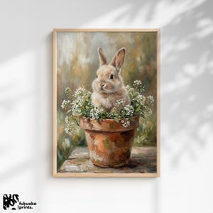 Pode incluir: Impressão emoldurada de um coelho marrom claro em um vaso de terracota cheio de flores brancas. A obra de arte tem um estilo suave e pictórico com uma paleta de cores neutras, evocando a primavera. Assinado por fukuoka | prints.