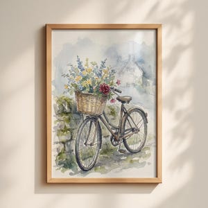 Pode incluir: Pintura em aquarela de uma bicicleta vintage com uma cesta de vime cheia de flores coloridas. A bicicleta está estacionada perto de uma parede de pedra, com uma pitoresca casa de campo ao fundo. A obra de arte é emoldurada em uma moldura de madeira clara.