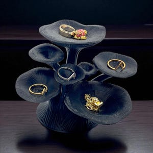 Peut inclure: Un présentoir à bijoux en forme de champignon bleu foncé avec plusieurs plateformes en forme de coupelles. Diverses bagues et un collier sont exposés sur les plateformes. Les bijoux comprennent des bagues en or et en argent, certaines avec des pierres précieuses.